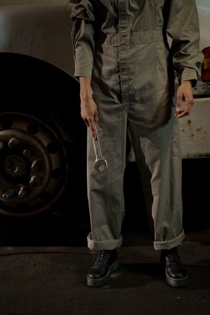 Mechanic in coverall with wrench standing by a vehicle wheel in an auto repair shop.